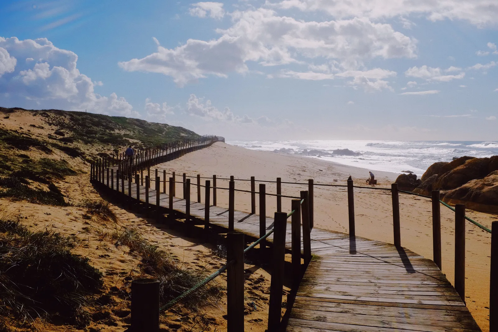 A wooden boardwalk running over the dunes beside a wide Atlantic surf beach