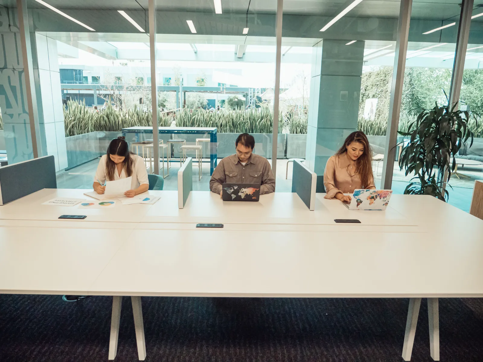 A coworking space with people working at laptops near large windows