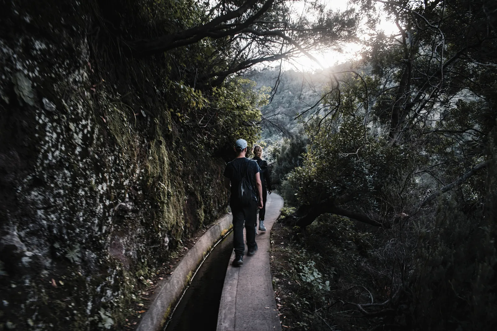 A narrow walking path beside a stone levada water channel running along a green mountainside in Madeira, Portugal