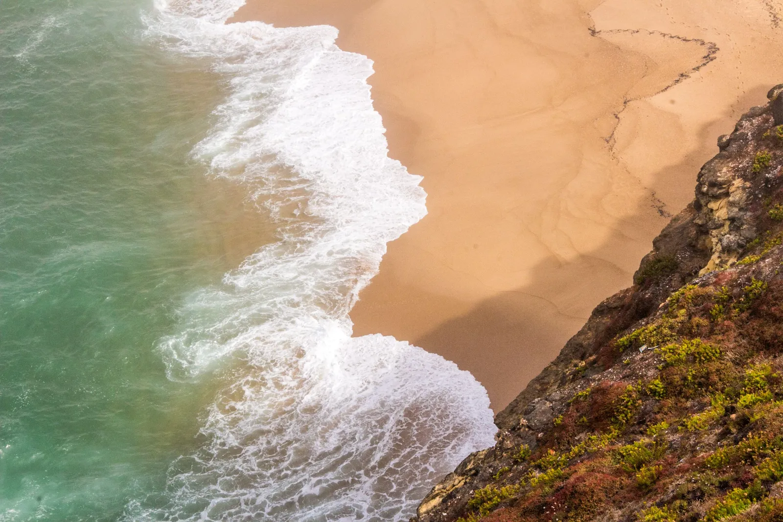 Atlantic surf breaking on the sand below the cliffs at Nazare, seen from above, Portugal
