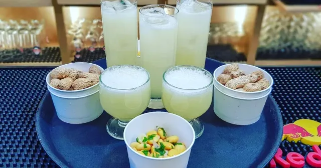 A round tray with glasses of a pale drink and small bowls of peanuts and lupini