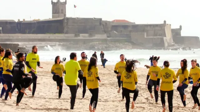 A group in yellow shirts warming up on the sand, a stone fortress behind
