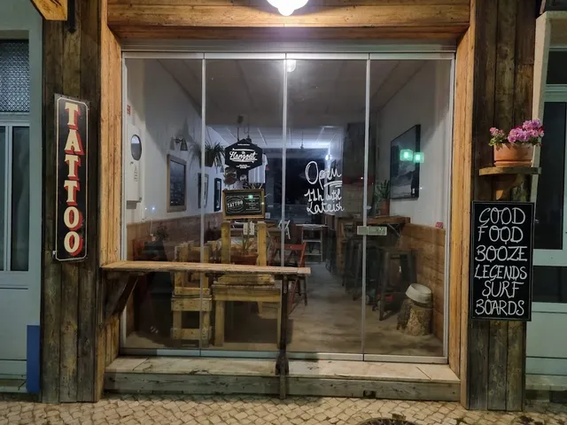 A wooden front with a wide glass window, a chalkboard and tables inside in the evening