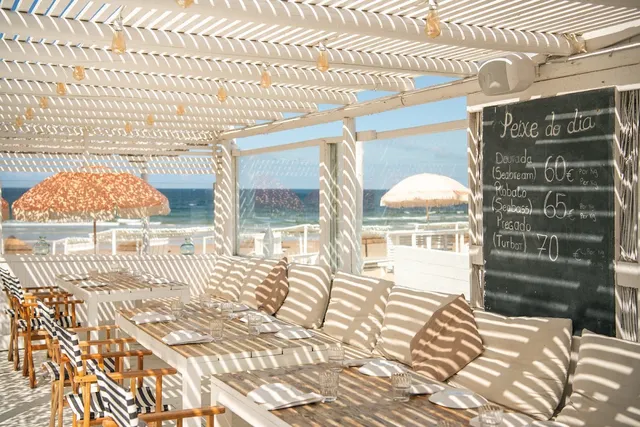 A terrace shaded by a white pergola with sofas, a catch of the day chalkboard and a sea view