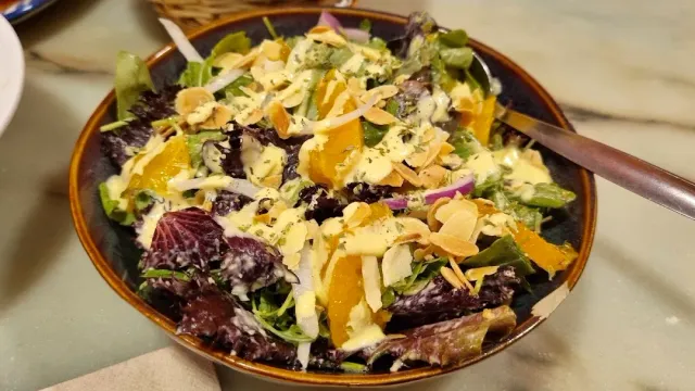 A bowl of leaf salad with orange segments, onion and sliced almonds