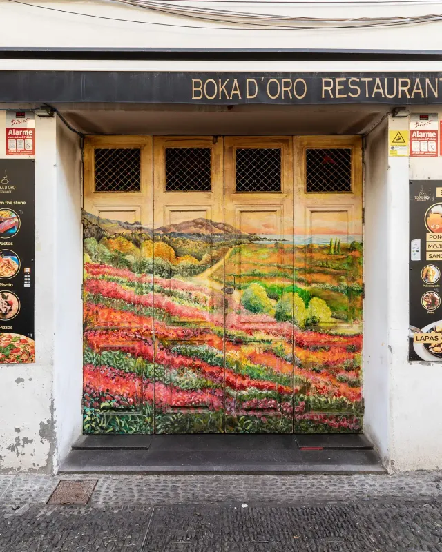 A wooden door painted with a colourful field landscape between menu boards