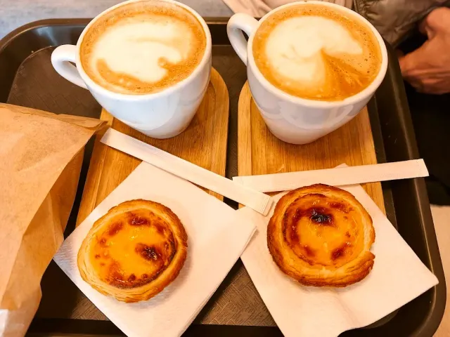 A metal tray with two cups of cappuccino and two custard tarts on wooden boards
