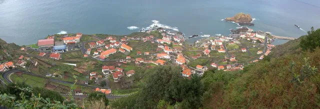 A panoramic view from above over a village of red roofs and a rocky bay on a cloudy day