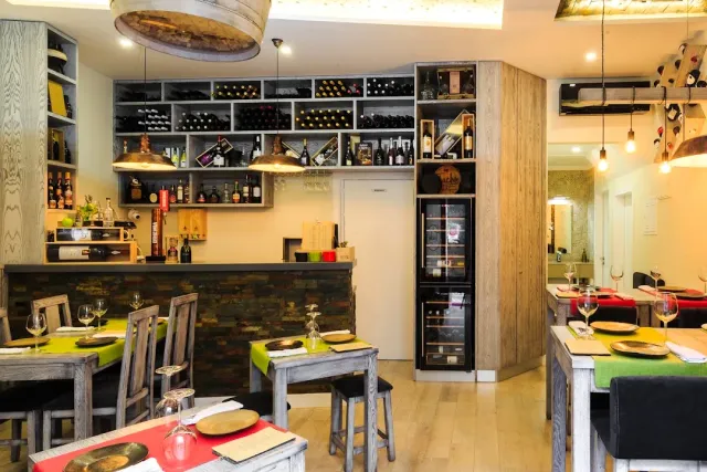 A counter with shelves of wine bottles, a wine fridge and tables with green cloths