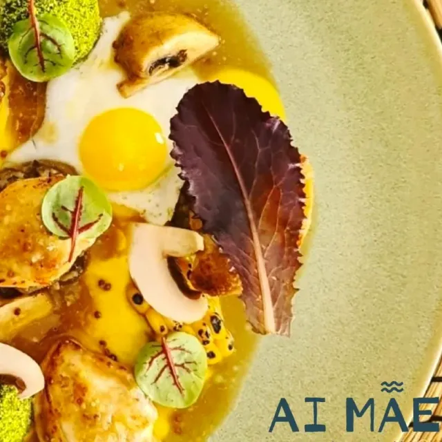 A close up plated dish with a fried egg, mushrooms, corn and leaves in a yellow broth