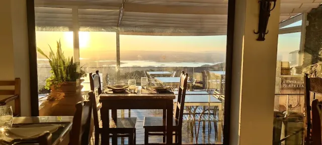 A set table by a large window onto a plain and a lake in sunset light