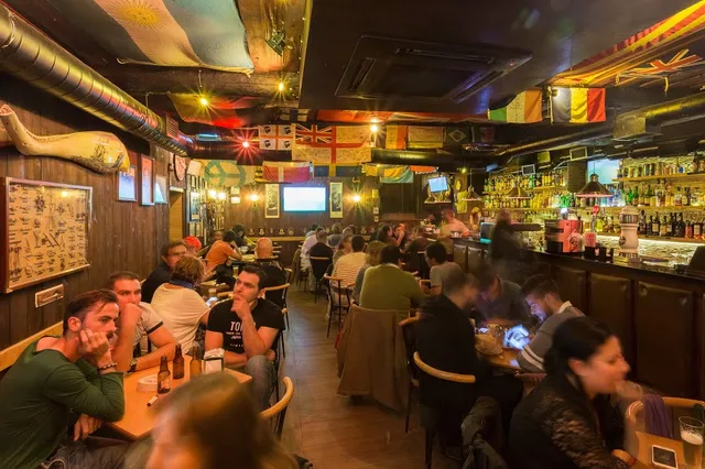 A busy pub with flags hanging from the ceiling, screens and a long bar along the wall
