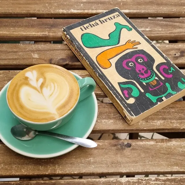 A green cup with a leaf drawn in the foam, on a slatted wooden table beside an old book