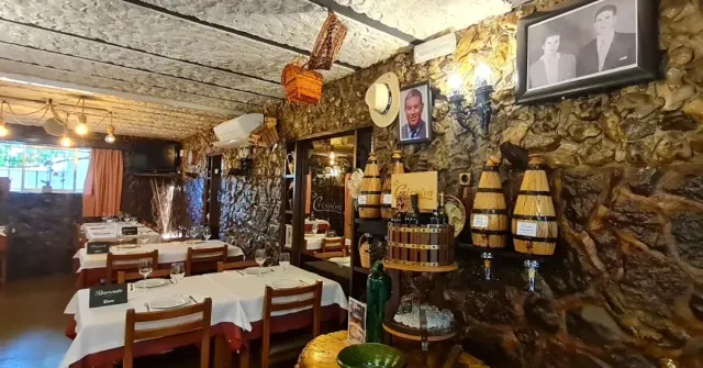 A room with rough stone walls, framed pictures, small barrels and white clothed tables