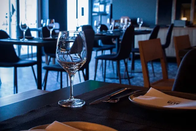 An empty wine glass on a set table in a dim space with dark chairs