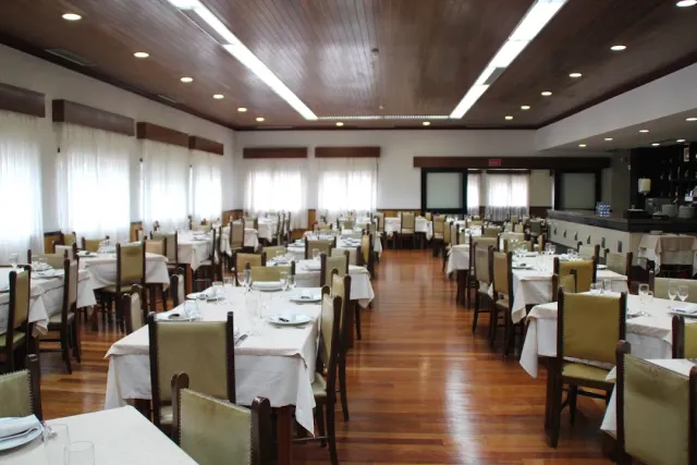 A wide room with a wooden ceiling, tables in white cloths and olive toned chairs