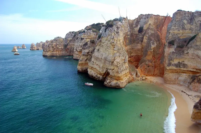 Golden sandstone cliffs dropping into turquoise water beside a narrow strip of sand