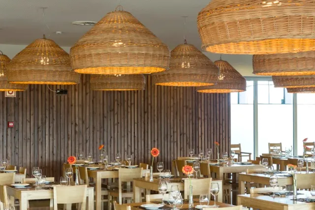 A spacious dining hall with large wicker lamps, a wooden wall and set tables