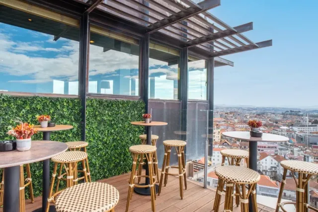 High stools beside an artificial plant wall on a rooftop with a view of the roofs