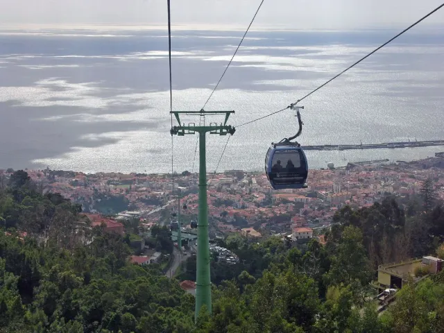 A cable car cabin gliding above city rooftops and a sea bay