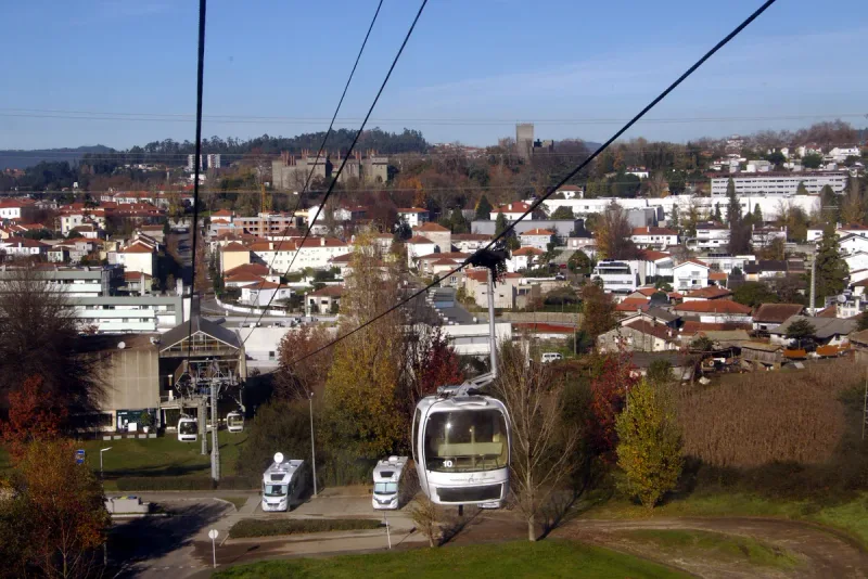 White cable car cabin descending over a town of tiled roofs with a hilltop castle behind