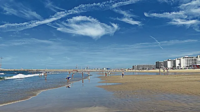 A wide strip of sand with bathers and a line of buildings behind