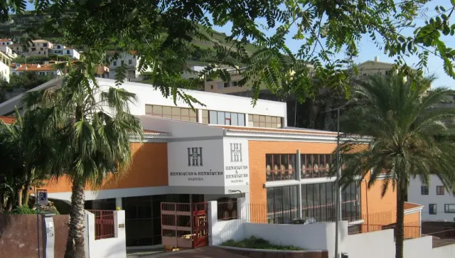 A white and orange winery building with signs, palm trees and a settled hillside behind