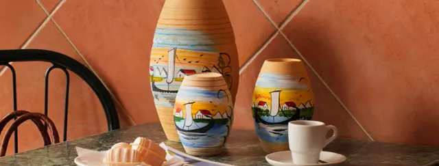 Three clay jars painted with boats on a marble table, an espresso cup and sweets