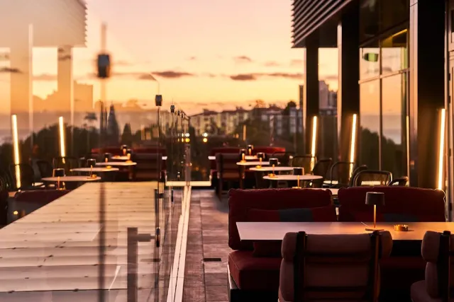 A terrace with red sofas and small tables facing an orange sunset sky