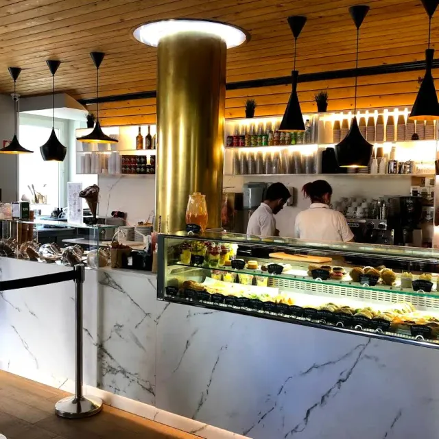 A marble counter with a pastry display, a brass column, black lamps and staff in white