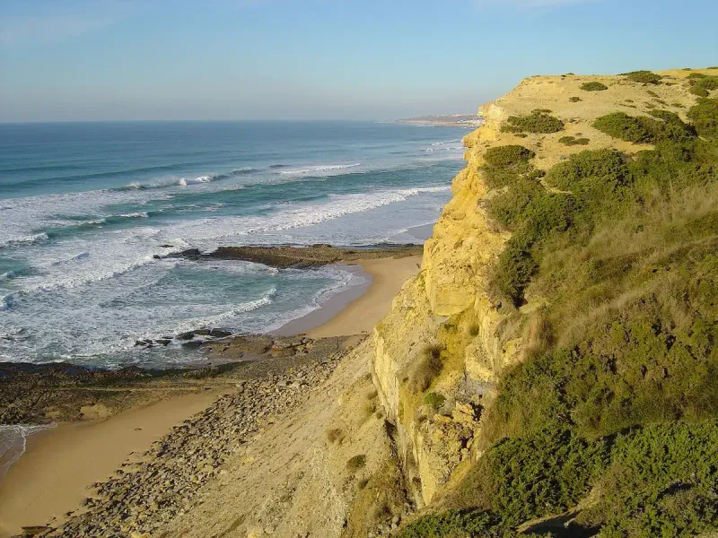 A sandy beach below an ochre sandstone cliff with waves breaking in lines