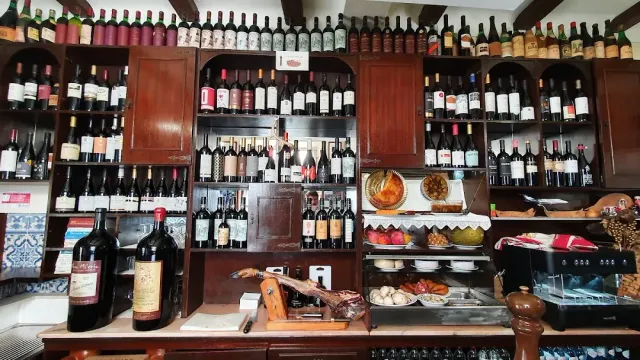 A wooden cabinet loaded with wine bottles above a counter with a ham leg and dishes