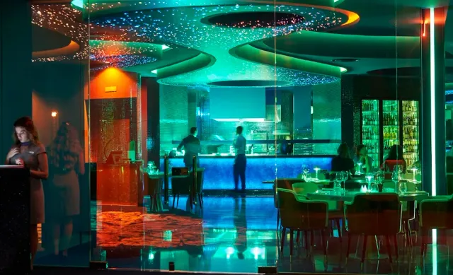 A space in green and red lighting with a starry ceiling and a lit bar counter