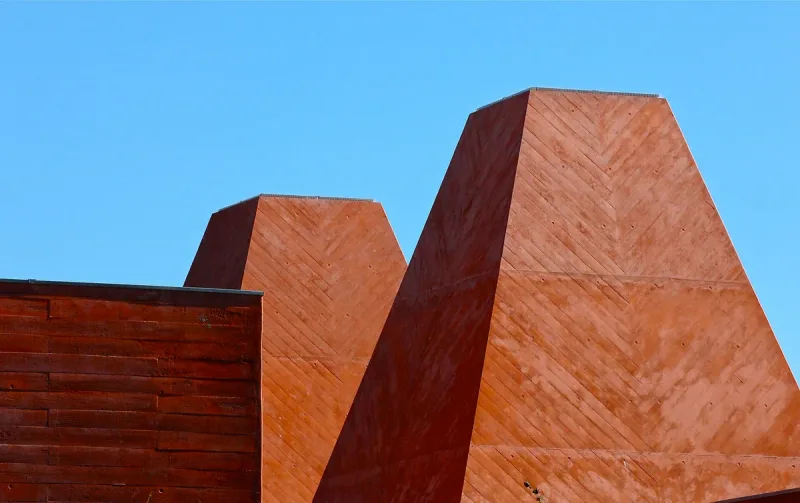 Two rust-red concrete pyramid towers against a blue sky