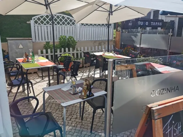 A paved yard with white parasols, colourful tables and a white wooden fence around