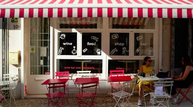 A shopfront with a red and white striped awning and red metal tables on the pavement