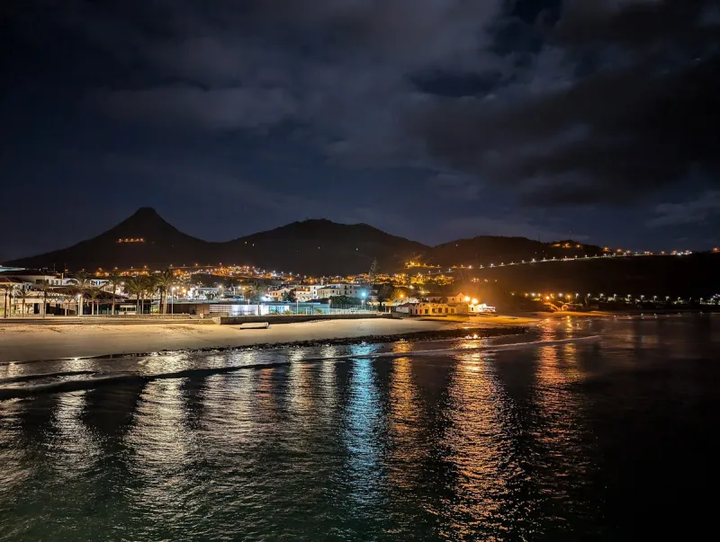 The sandy beach of Porto Santo at night, town lights reflected in the water and hills on the horizon