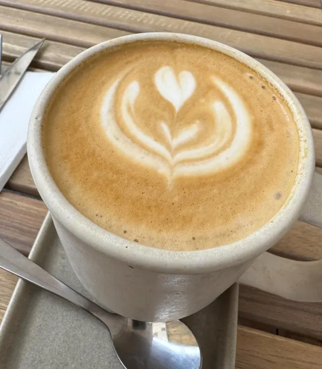 A pale cup with a leaf drawn in the milk foam, on a tray beside a wooden table