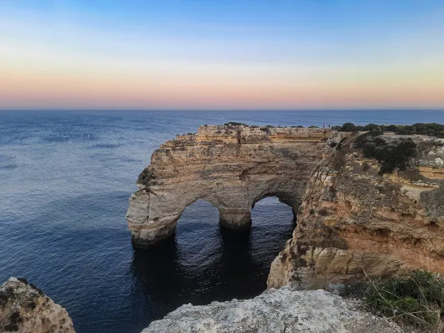A double rock arch in the sea below limestone cliffs, seen from above at dusk