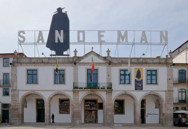 A white arcaded warehouse with a giant sign and a black caped figure on the roof