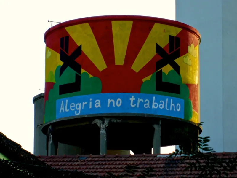 Round water tower painted with a stylised sun and lettering on a blue band above tiled roofs
