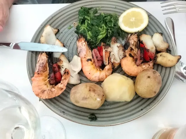 A plate with grilled prawns, calamari, spinach, potatoes and a lemon wedge