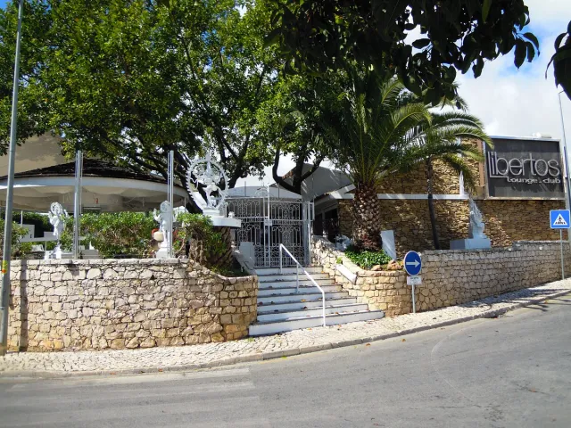A white building behind a stone wall, steps, white statues and palm trees