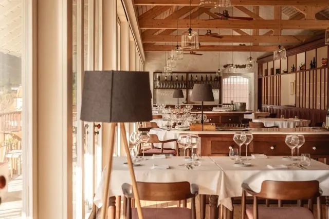 A room with wooden roof beams, white tablecloths and a large floor lamp