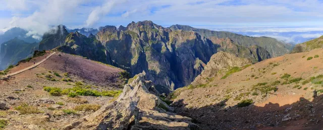 Sharp rocky mountain ridges with a trail climbing between the peaks