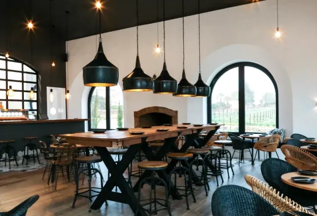 A long wooden table under black pendant lamps, and an arched window onto a green field