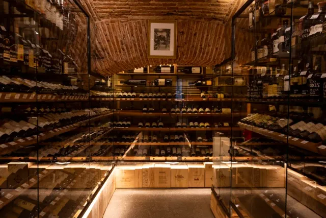 A brick vaulted cellar with lit glass cabinets full of wine bottles
