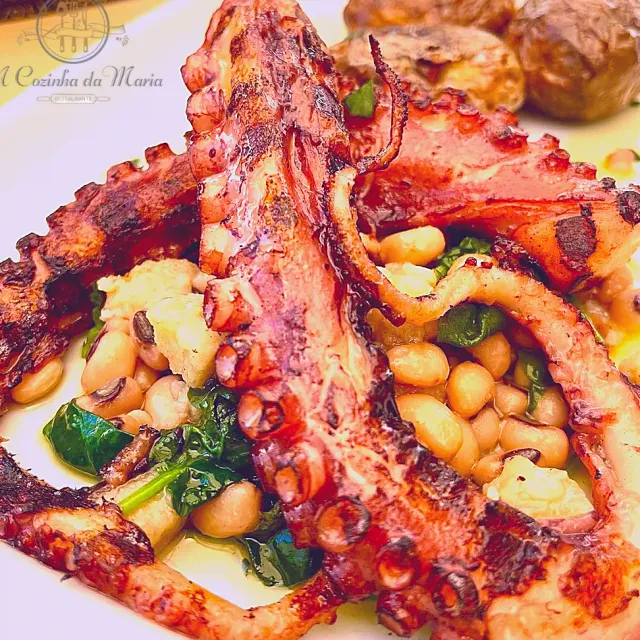 A close up of grilled octopus over white beans, green leaves and potatoes