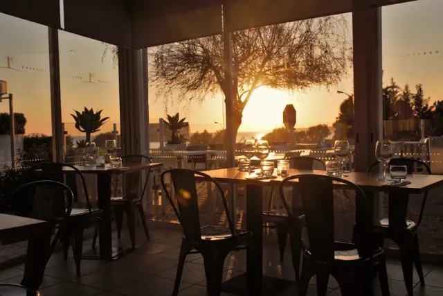 Black metal tables and chairs facing a wide window with a sunset behind a tree