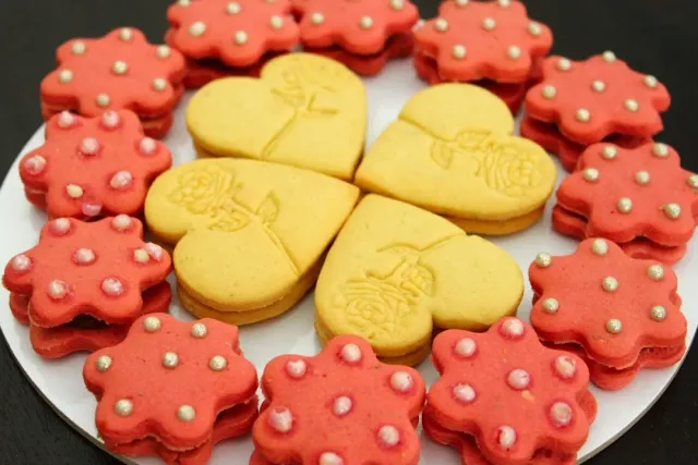 A plate of pink and yellow heart and flower shaped biscuits decorated with sugar pearls